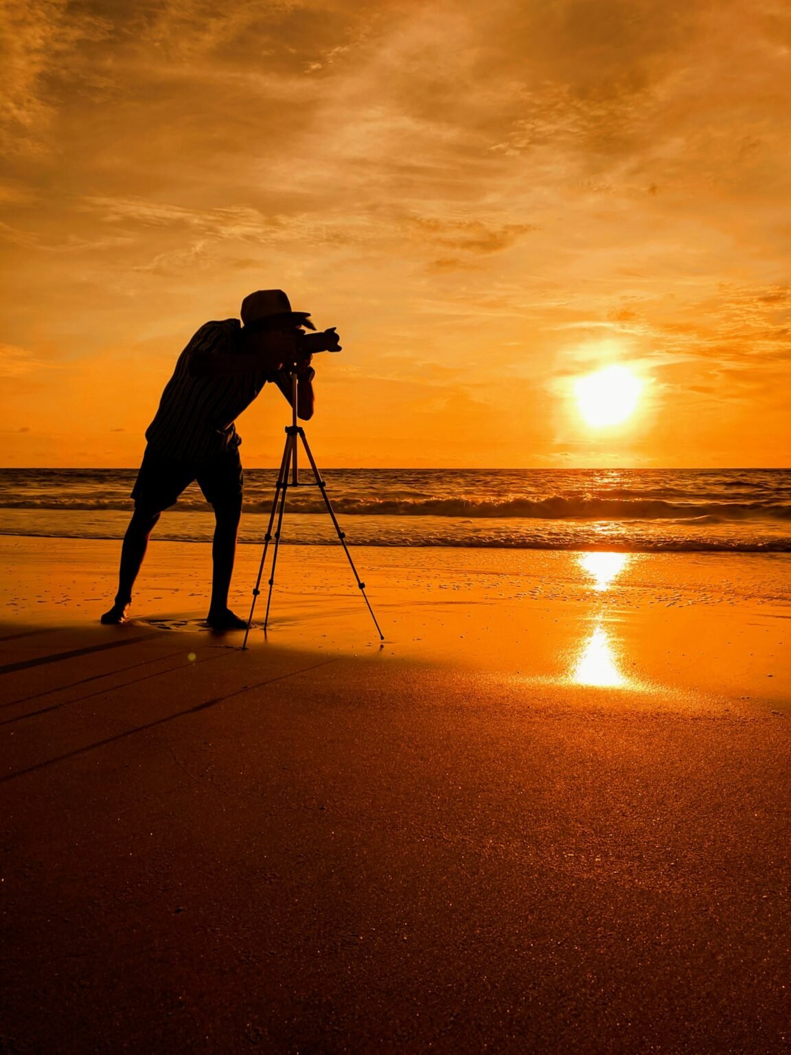 مصور يستخدم كاميرا على حامل ثلاثي أمام مشهد غروب عالي التباين مناسب لتقنية Exposure Bracketing