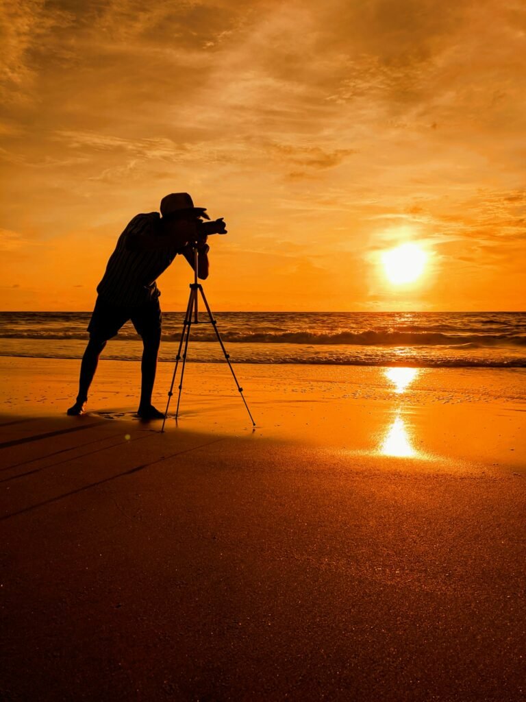 مصور يستخدم كاميرا على حامل ثلاثي أمام مشهد غروب عالي التباين مناسب لتقنية Exposure Bracketing